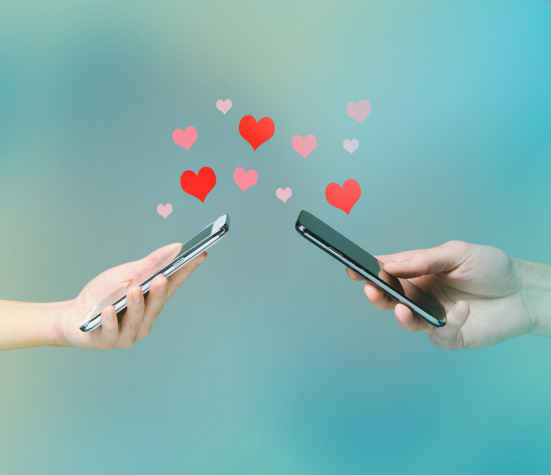 Young man and woman's hands holding smart phones with hearts floating over