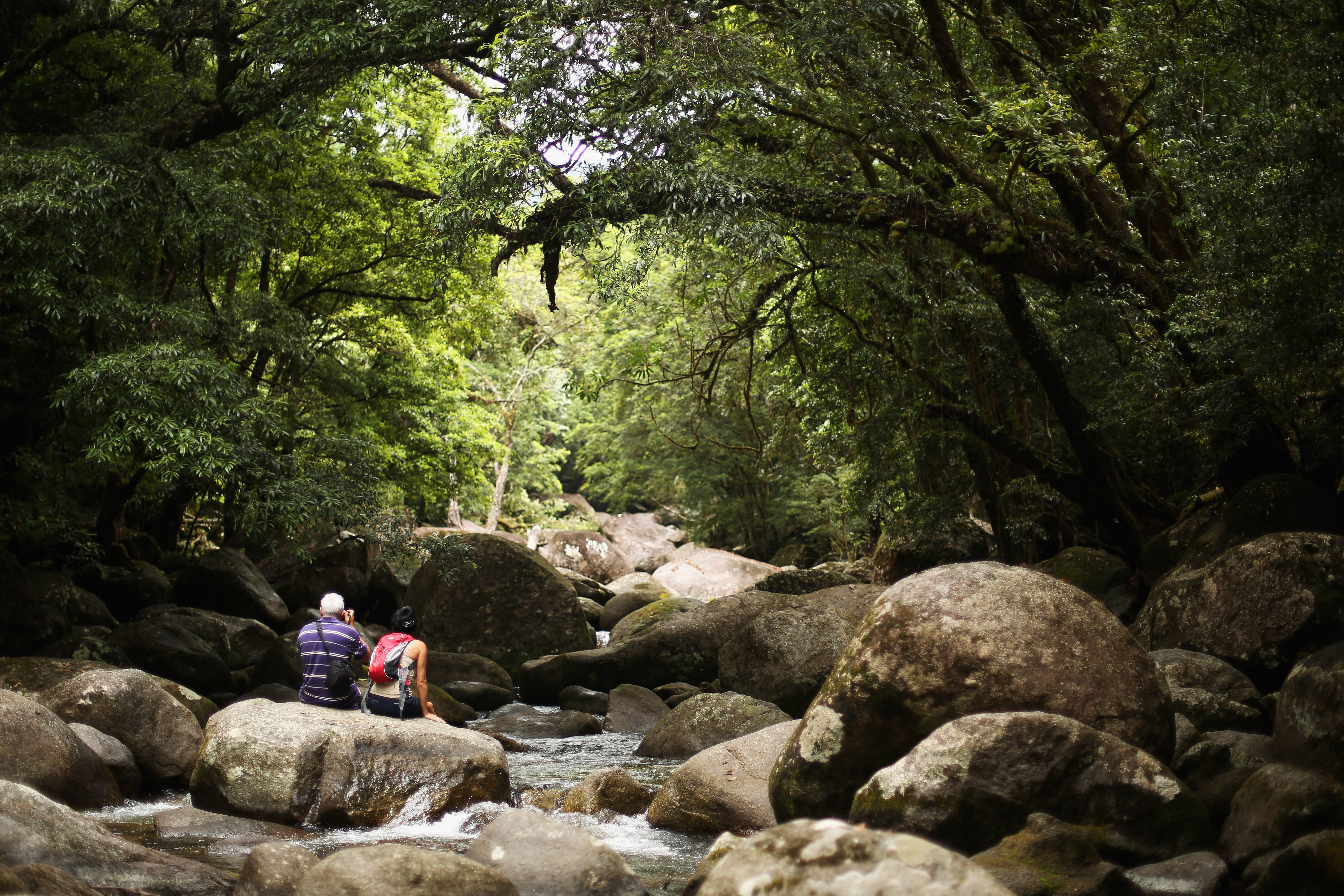 CAIRNS, AUSTRALIA - NOVEMBER 15:  A couple sit on the rocks of the Mossman river in world heritage listed daintree rainforest on November 15, 2012 in Mossman Gorge, Australia. Located in Far North Queensland, the Cairns region is one of Australia’s most
