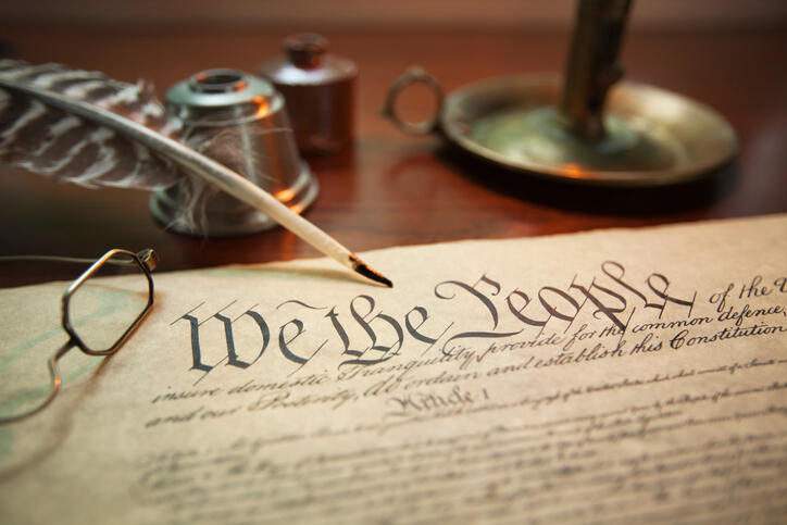 Selective focus image of the United States Constitution with quill pen, glasses and candle holder