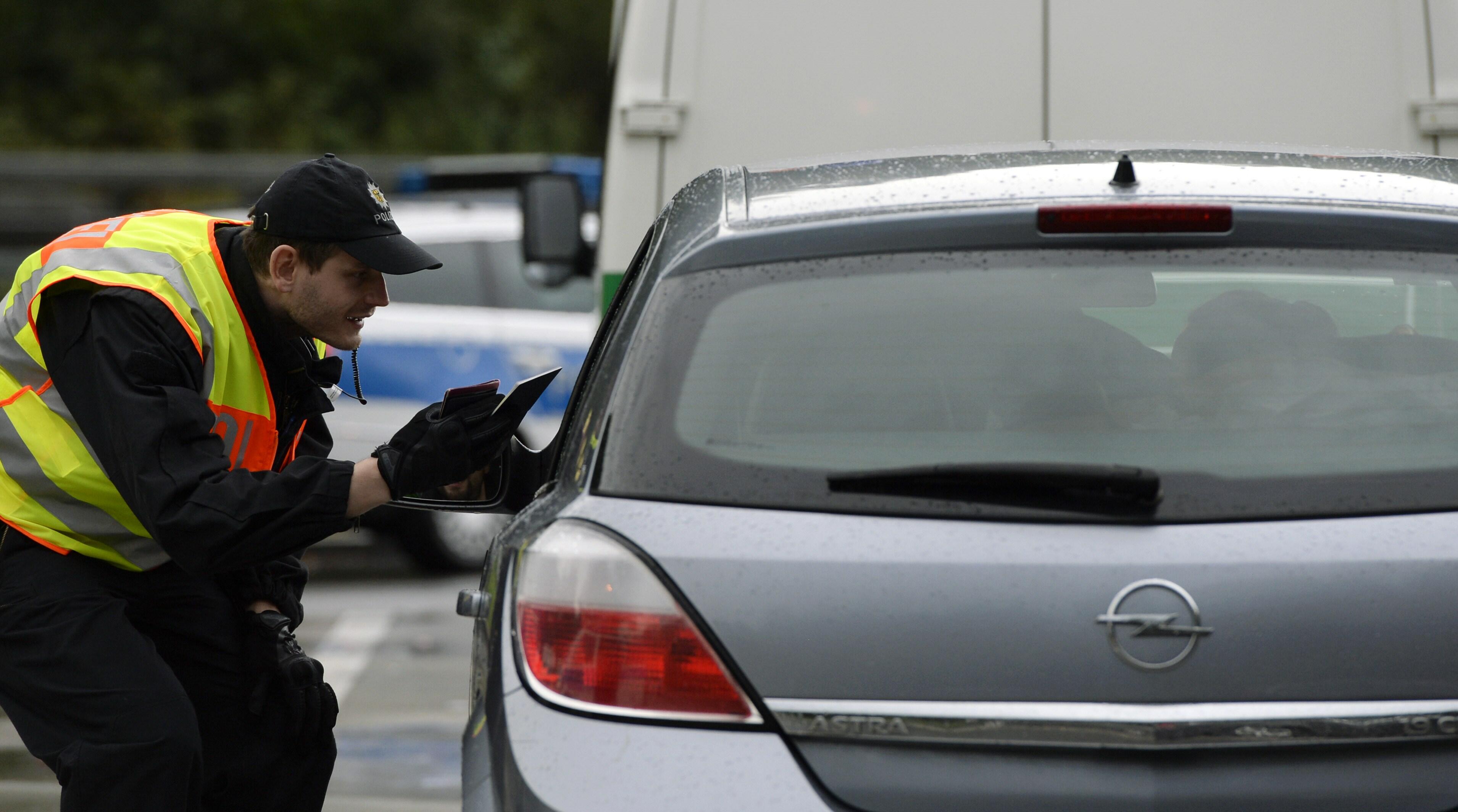 A police officer controls a car at a parking spot at the German-Austria border, near the village of Passau, southern Germany, on September 14, 2015. Honking cars with stressed drivers banked up for kilometres (miles) at an Austrian-German road crossing Mo