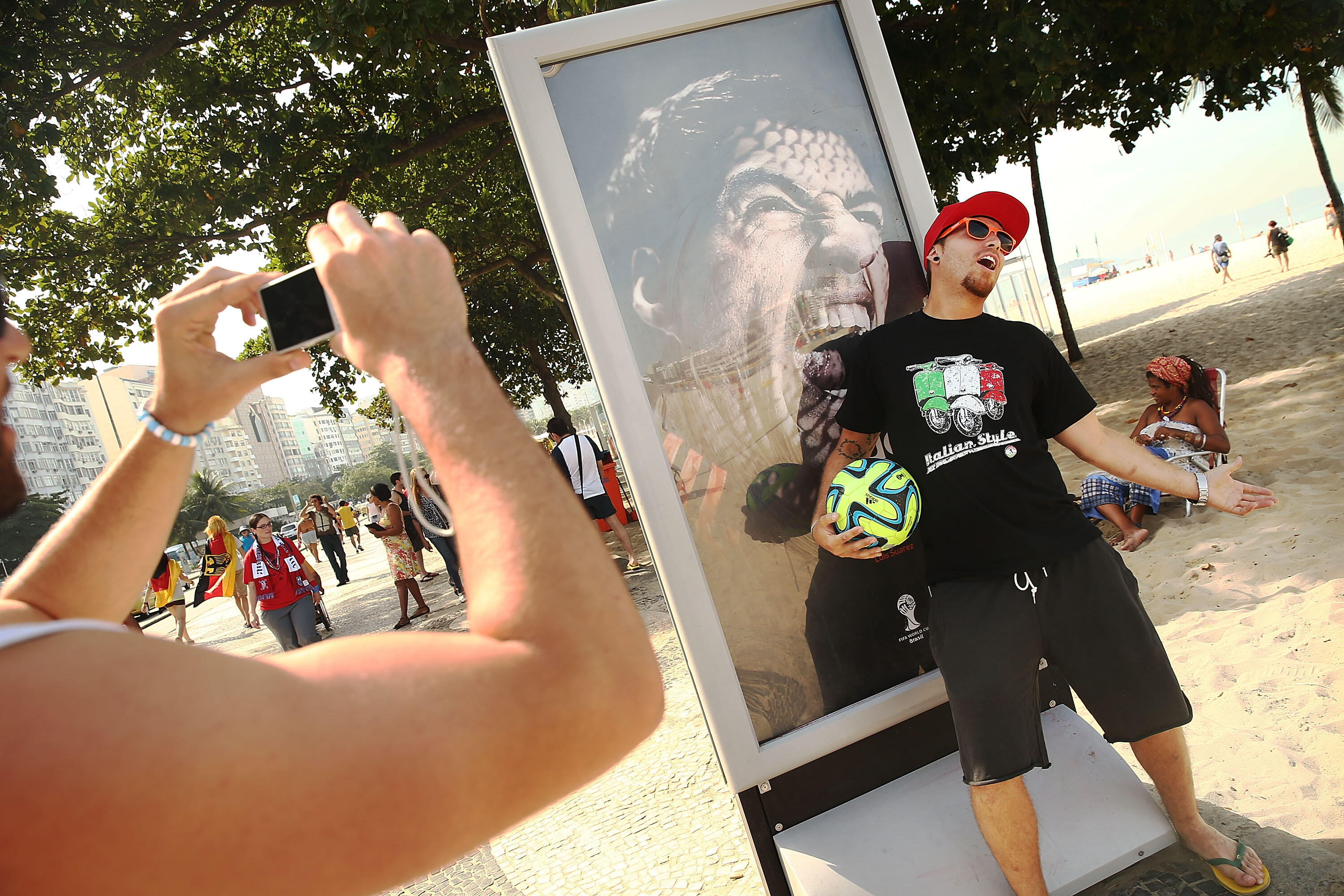 RIO DE JANEIRO, BRAZIL - JUNE 26:  A man taks a photo next to an advertisement featuring Uruguay's Luis Suarez, mocking the biting incident against opponent Giorgio Chiellini during the World Cup match against Italy, on Copacabana Beach on June 26, 2014 i