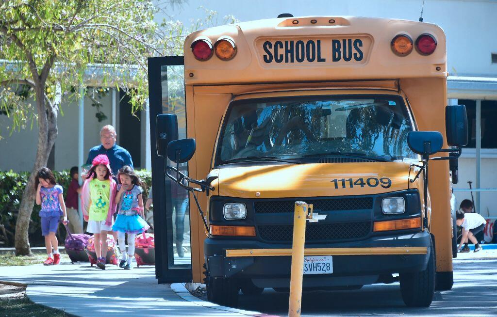 Children walk past a School Bus in Monterey Park, California on April 28, 2017.  In some schools, children are forced to mop cafeteria floors. In extreme cases, students are sent home with a stamp on their arm that reads 
