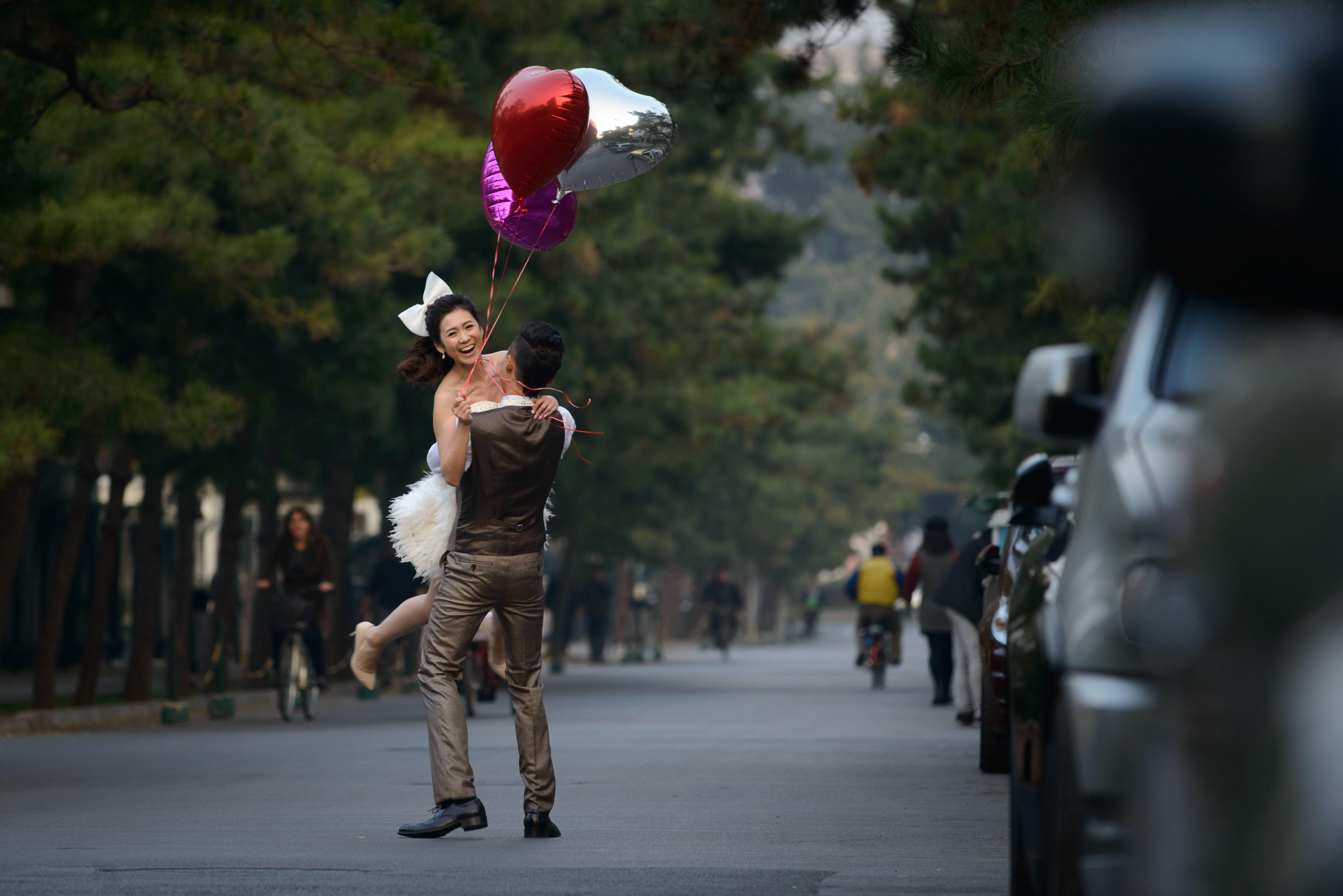 A woman wearing a wedding dress and holding heart-shaped ballons is lifted by a man on a street in Beijing on October 21, 2013. China's gross domestic product expanded 7.8 percent year-on-year in July-September, data showed, snapping two quarters of slowi