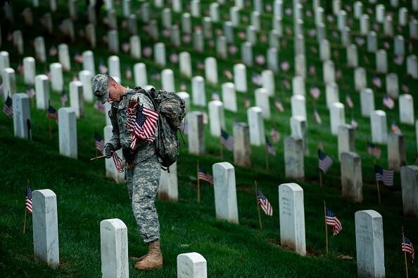 A soldier in the Old Guard places flags at graves in Arlington National Cemetery during 