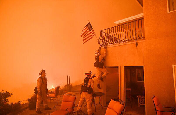 Firefighters save a US flag as impending flames from the Wall fire close in on a luxury home in Oroville, California on July 8, 2017. At least 10 structures have burned and the fire is currently at 20 percent containment. The first major wildfires after t