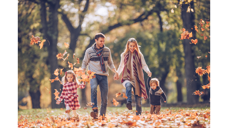 Young happy family holding hands and having fun with autumn leaves at the park.
