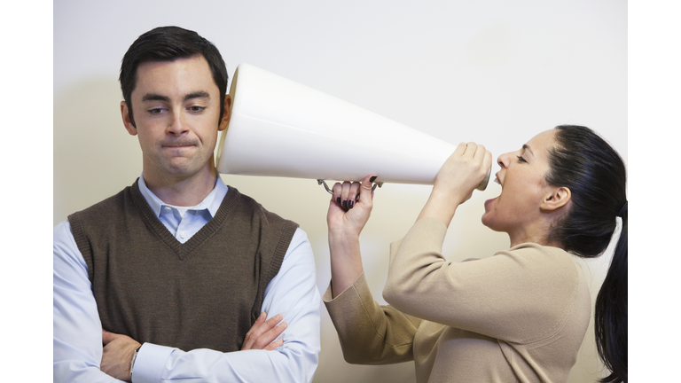 Businesswoman shouting with megaphone into co-worker's ear