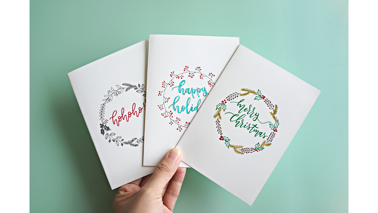 Cropped Hand Holding Christmas Cards With Text Over Turquoise Background