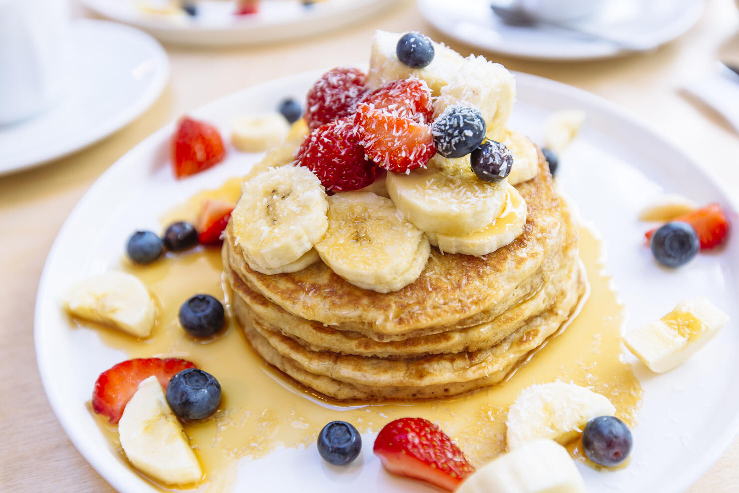 Close-up of delicious pancakes with fresh fruits, berries and maple syrup on a plate