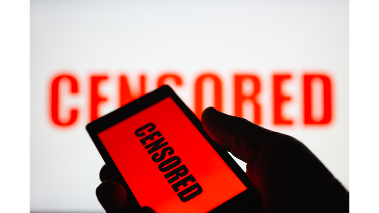 A smartphone in hand displaying the "censored" text. Same text in red blurred on white background. The concept of censorship on popular social networks. Restricted access to internet. Shallow DOF