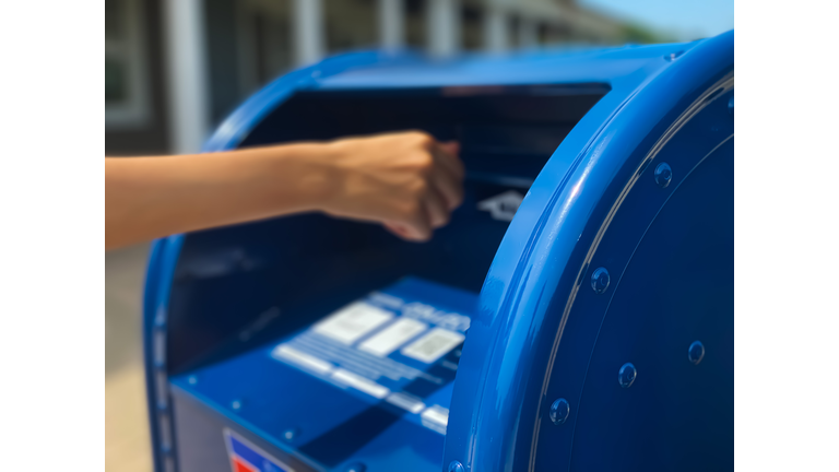 side profile view of mixed-race female mailing letter at traditional blue postal mailbox