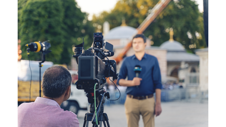 Behind the scene concept. Cameraman working on professional camera taking TV interviewer, professional news reporter making news outdoors.