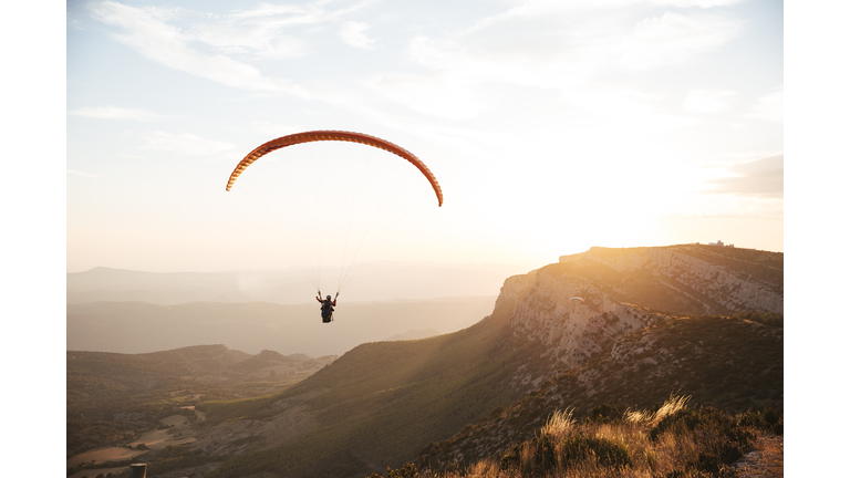 Spain, Silhouette of paraglider soaring high above the mountains at sunset