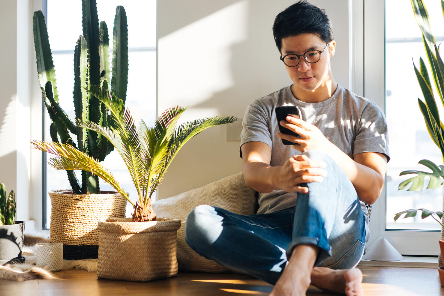 Young Man Using Smartphone At Home With Plants