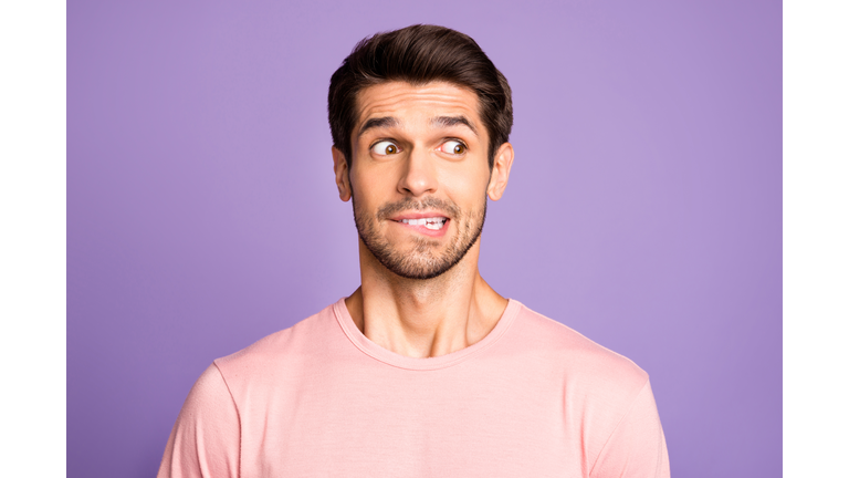 Close-up portrait of his he nice attractive funny confused brunet bearded guy wearing pink tshirt waiting news biting lip isolated over violet purple lilac pastel color background