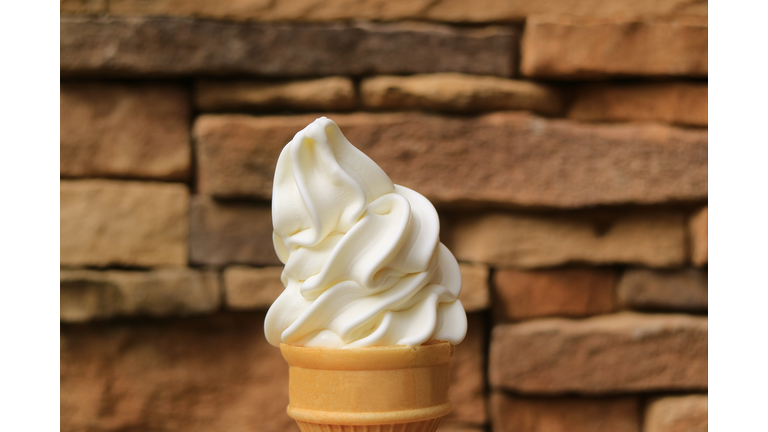 Mouthwatering Vanilla Soft Serve Ice Cream Cone Against Blurry Brown Stone Blocks Wall