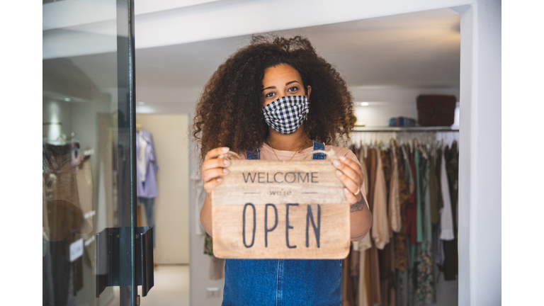 Woman holding Open sign in a small business boutique shop after Covid-19 pandemic