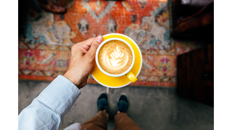 Man holding yellow cup with cappuccino, personal perspective view