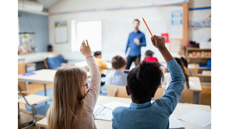 Rear view of students sitting with hands raised in classroom