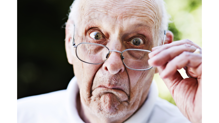 Grumpy old man looks over spectacles, shocked and disapproving