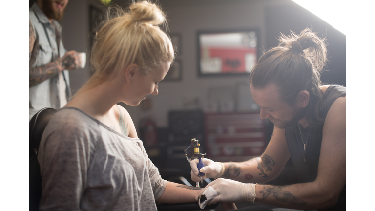 Artist making tattoo on female customer's hand
