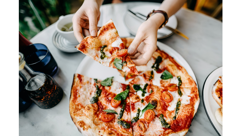 Overhead view of woman's hand getting a slice of freshly made pizza and enjoying her meal in an Italian restaurant