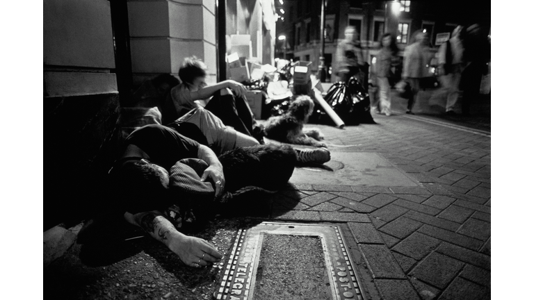 Homeless people with dogs huddled together on pavement, night (b&w)