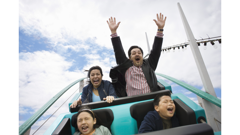 Family riding rollercoaster, father with hands up in air