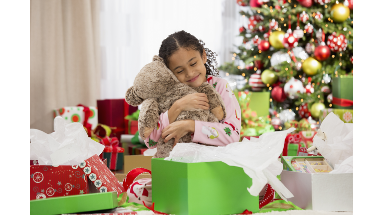 Hispanic girl hugging teddy bear Christmas gift