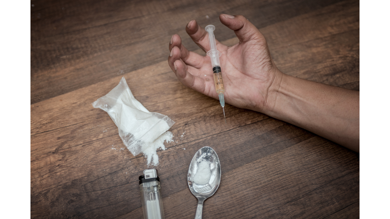 Unconscious drug addict hands lying on grungy concrete floor with pills, syringe, cooked heroine. Dangers of drug addict and abuse concept. International Day against Drug Abuse.