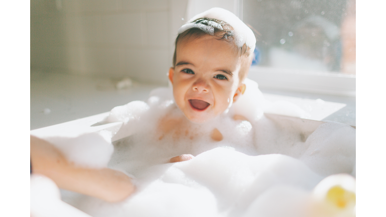 Cute Happy Baby Boy Taking Bubble Bath In Kitchen Sink At Home