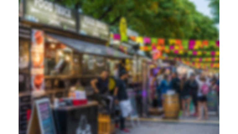Food trucks and people at a street food market festival on a sunny day, blurred on purpose