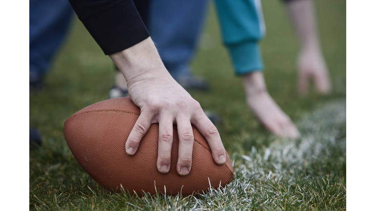 Close up of a hand holding an oval football on the line, during a game of non-contact flag football.