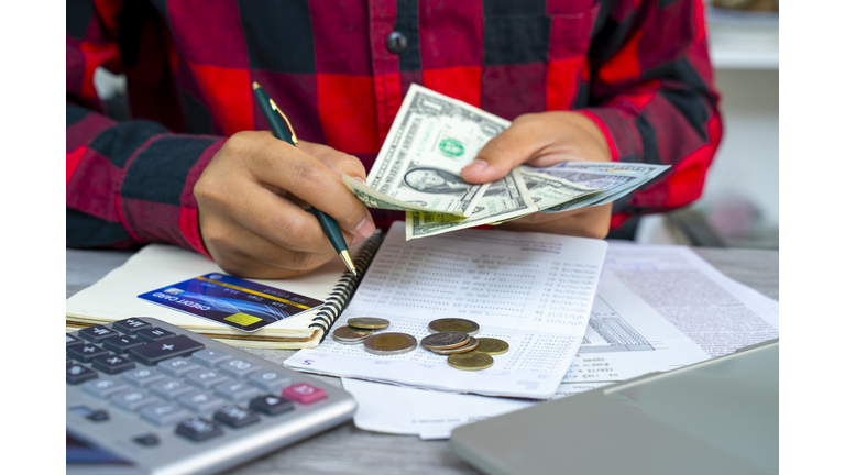 Expense and budget concept, woman hand holding Euro banknote money with list of expense in small notepad and calculator on wooden table.