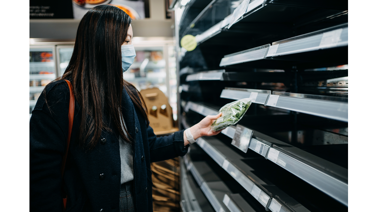 Young Asian woman with surgical face mask shopping for vegetables in front of empty shelves in a supermarket after panic buying due to the outbreak of coronavirus