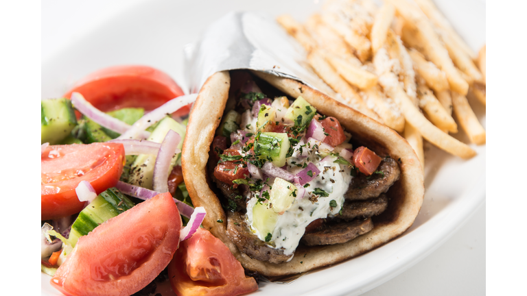A close-up of a gyro pita sandwich with a salad and fries.