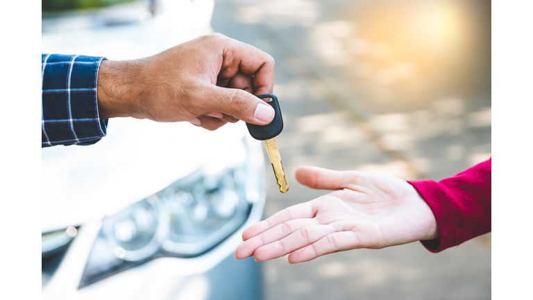 Close up hand male giving a key new car on hand female outside her car. Concept of rent car or buying car.