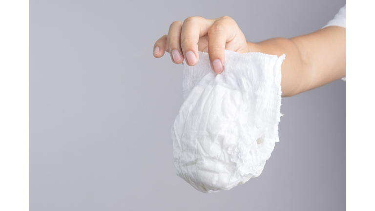 Cropped Hand Of Person Holding Diaper Against Gray Background