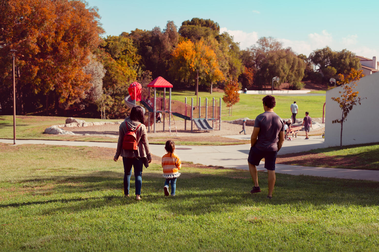 Family With Toddler Daughter Walking Toward A Park Playground