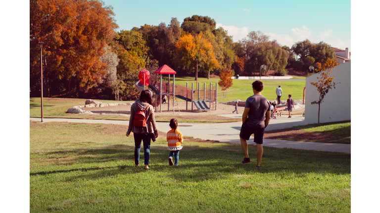 Family With Toddler Daughter Walking Toward A Park Playground