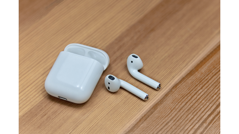 Mobile airpods on wooden blurred background. Apple wireless earphones with charger box, chosen focus.
