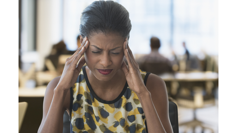 Anxious mixed race businesswoman rubbing temples in office