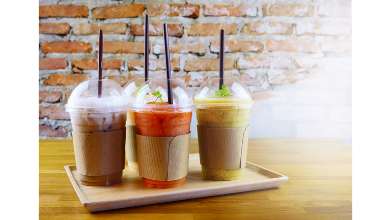 Smoothies and iced coffee in plastic cup on wooden tray and brick wall background in cafe. Take away drinks concept.