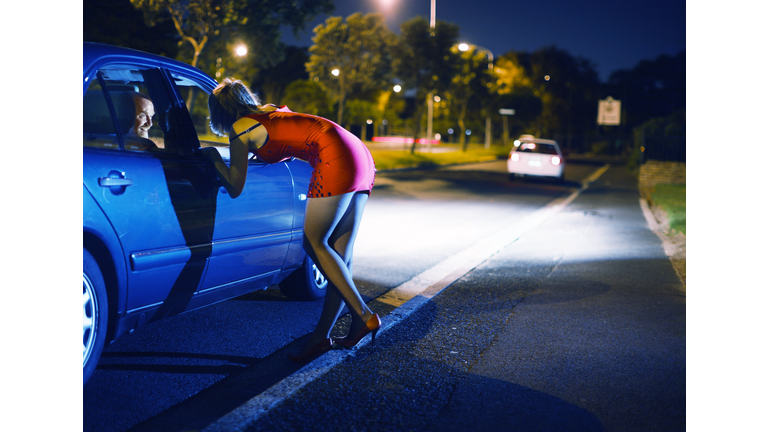 Young prostitute wearing red propositions man in car