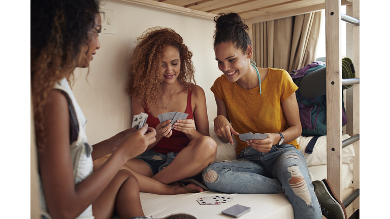 Young women playing cards in bunk bed, at youth hostel