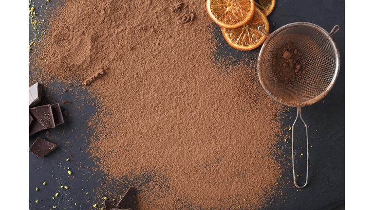 Sifted cocoa powder in a sieve over black background