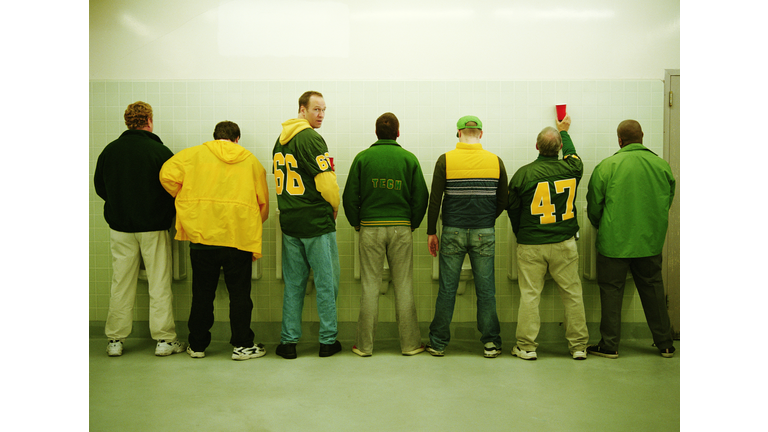 Men lined up at urinal, one looking back