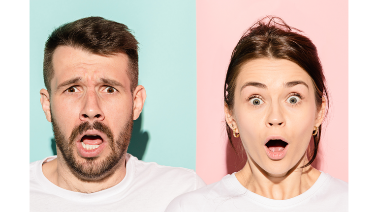 Closeup portrait of young couple, man, woman. One being excited happy smiling, other serious, concerned, unhappy on pink and blue background. Emotion contrasts