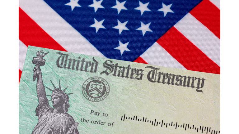 United States Treasury check and American flag. Concept of stimulus payment, tax refund. Federal government grants, loans, benefits and assistance