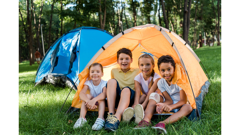 happy multicultural kids smiling while sitting in yellow camp